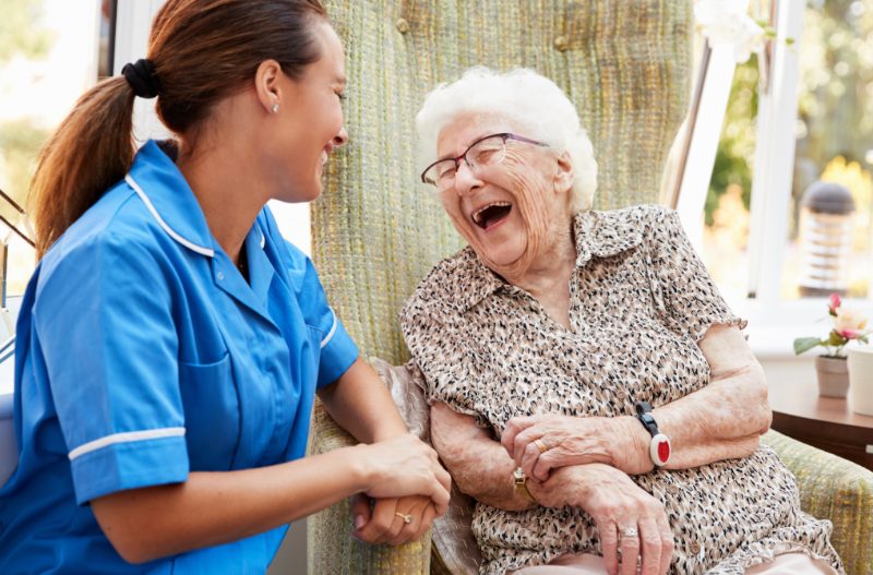 Caregiver laughing with an older woman in her chair at home