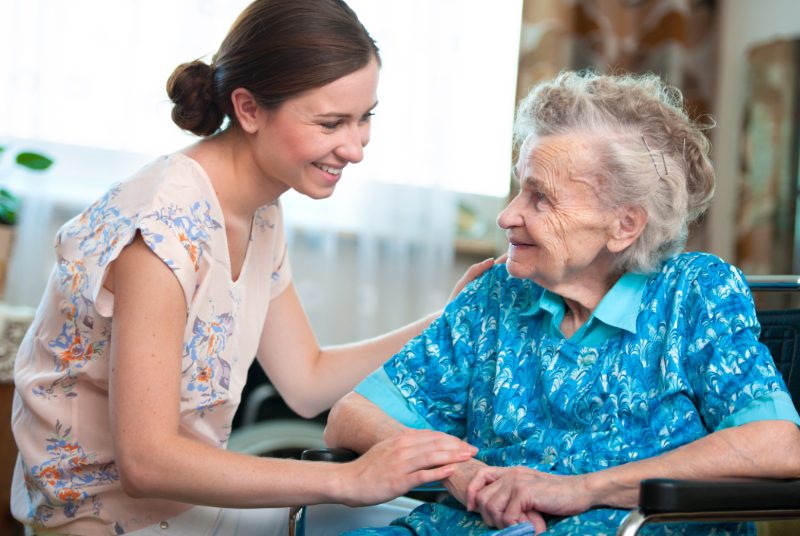 Caregiver smiling with an older woman seated in a wheelchair